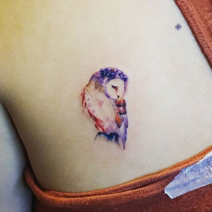 Colorful small bird tattoo on skin with watercolor style detailing.