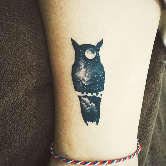 Small bird tattoo with a celestial theme, featuring an owl silhouette filled with stars and a moon on the leg.