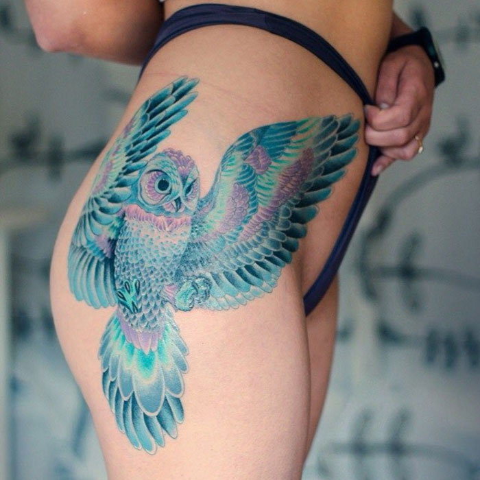Colorful small bird tattoo of an owl on the side of a person's body, showcasing intricate details and vibrant hues.