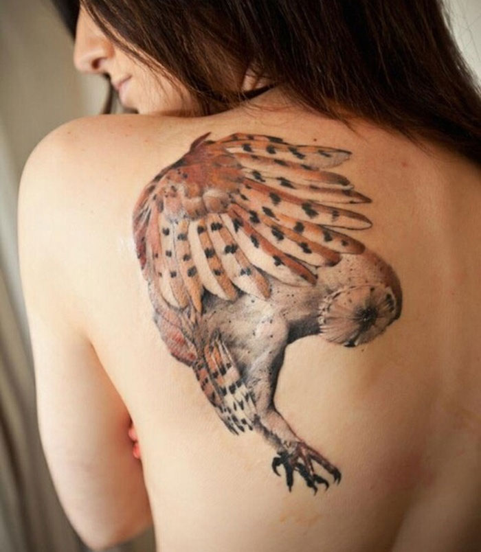A detailed small bird tattoo on a person's shoulder showcasing intricate feather patterns.