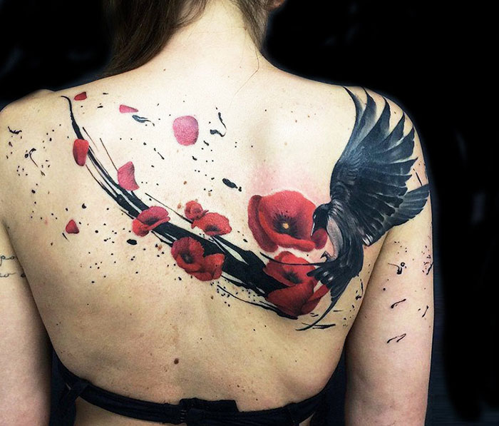 Unique small bird tattoo with red flowers on a woman's back.