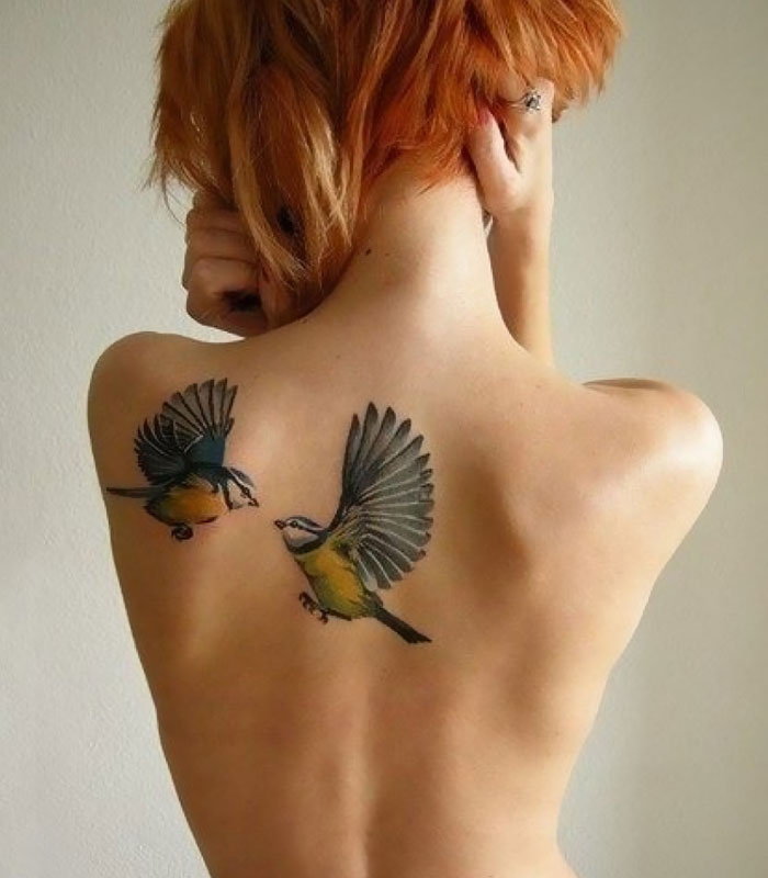 Unique small bird tattoos on a person's back, featuring two colorful birds in flight.
