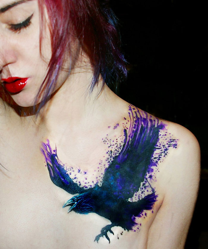 Woman with a vibrant purple and black small bird tattoo on her chest.
