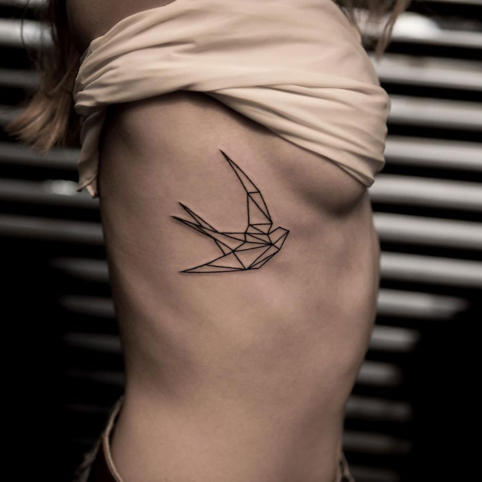 Geometric small bird tattoo on a person's side, featuring minimalist black line design.