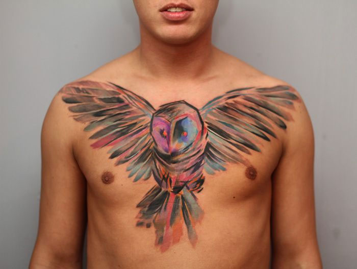 Colorful small bird tattoo on a man's chest, showcasing vibrant ink artistry.