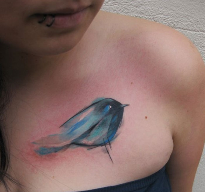 Watercolor small bird tattoo on chest, showcasing unique tattoo artistry.