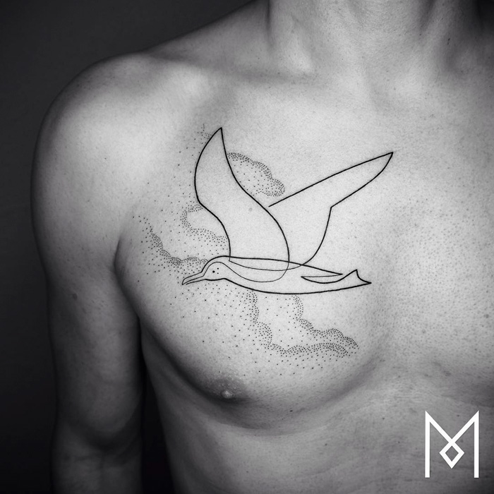 Minimalistic small bird tattoo on chest, featuring sleek line art and dotted clouds.