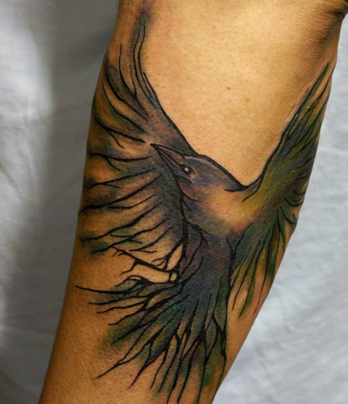Small bird tattoo on forearm with detailed wing design, black and green hues.
