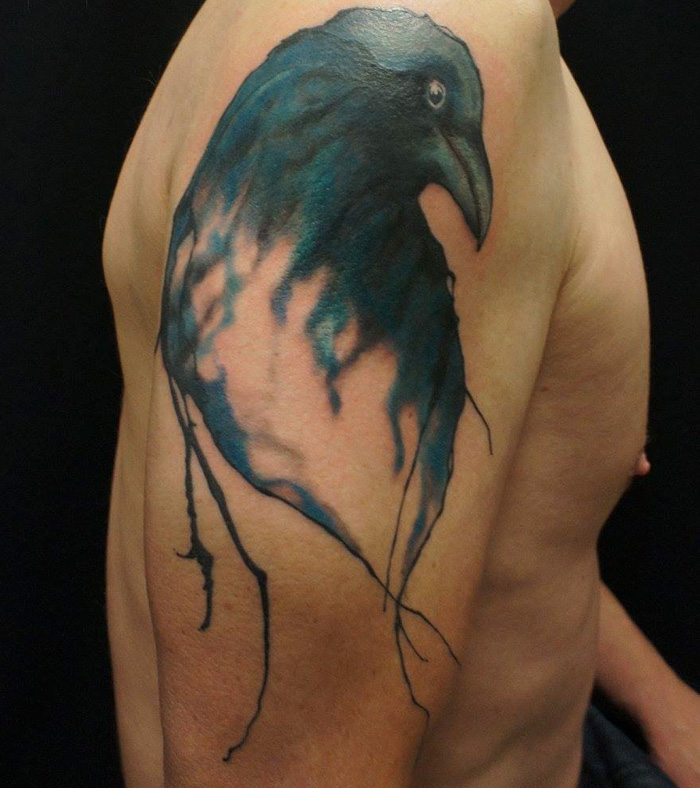 Unique small bird tattoo in vibrant blue on a person's upper arm, showcasing detailed and artistic inkwork.