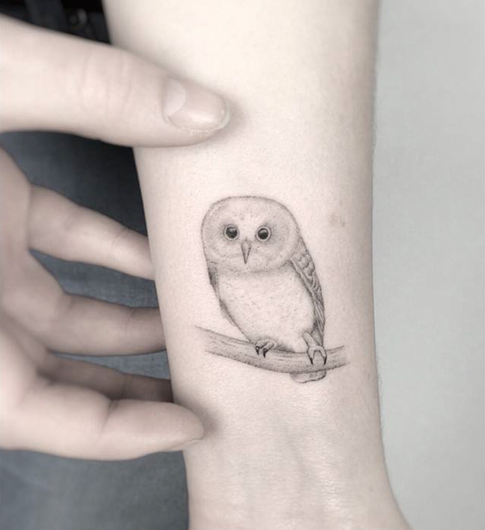 Small bird tattoo of an owl on a forearm, showcasing detailed and delicate ink art.