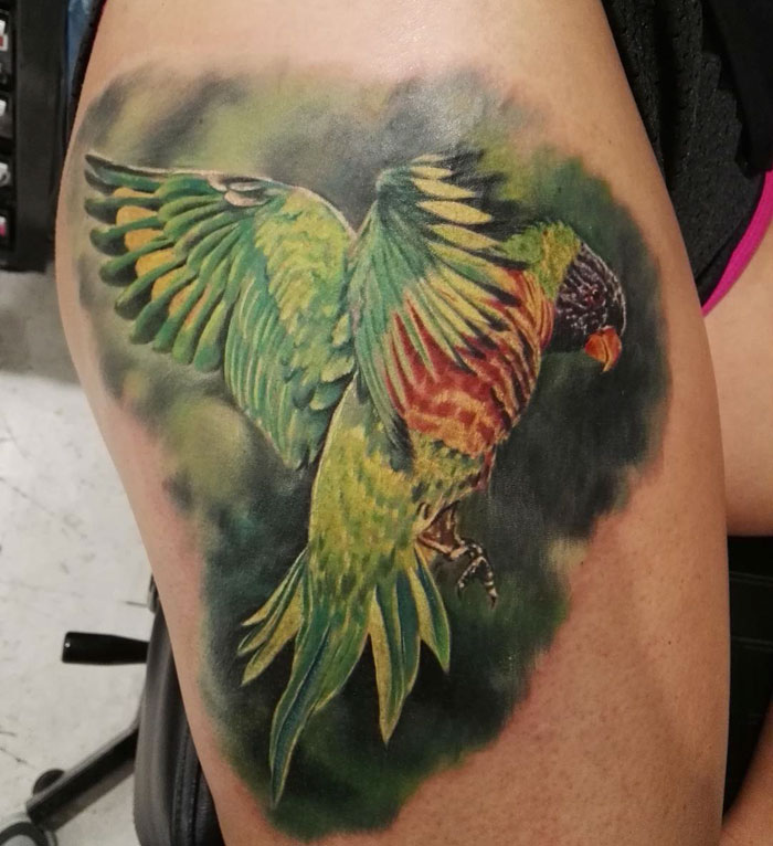 Colorful small bird tattoo with vibrant green, yellow, and red feathers on skin.