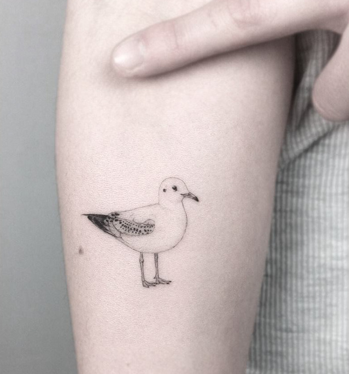 Minimalist small bird tattoo on arm, showcasing delicate ink details and unique design inspiration.