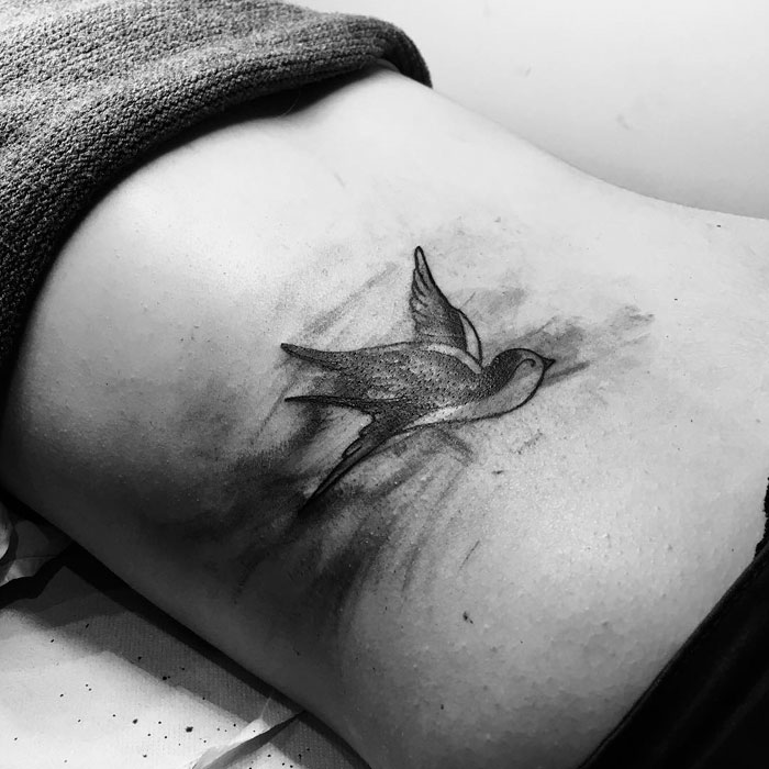 Black and white small bird tattoo on side of body, showcasing intricate design and shading details.