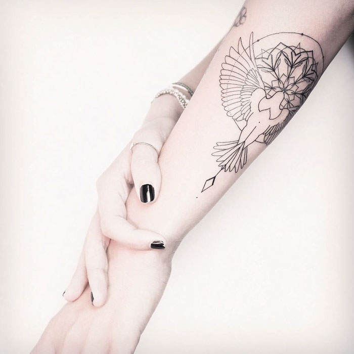 Unique small bird tattoo on forearm, featuring intricate geometric designs.
