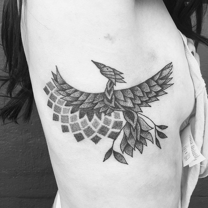 Unique small bird tattoo design with intricate patterns on a person's side.