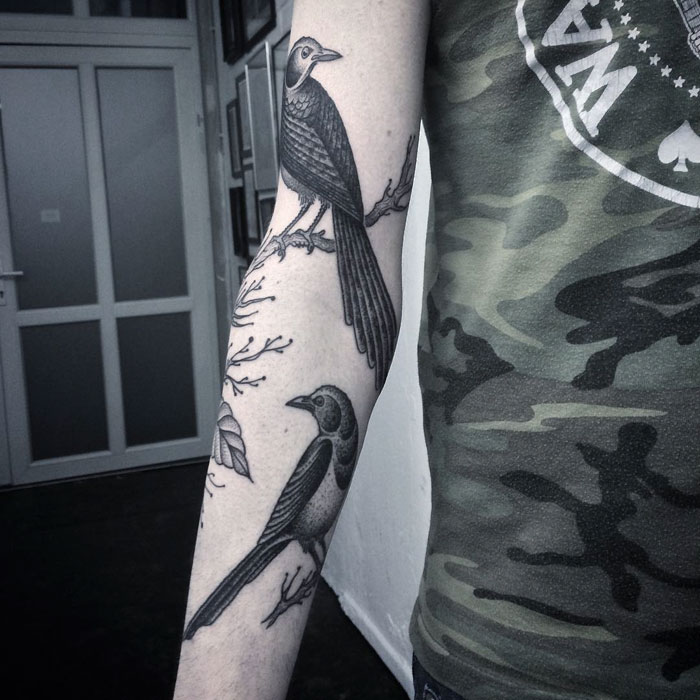 Small bird tattoos on arm, featuring intricate black ink designs with nature elements.