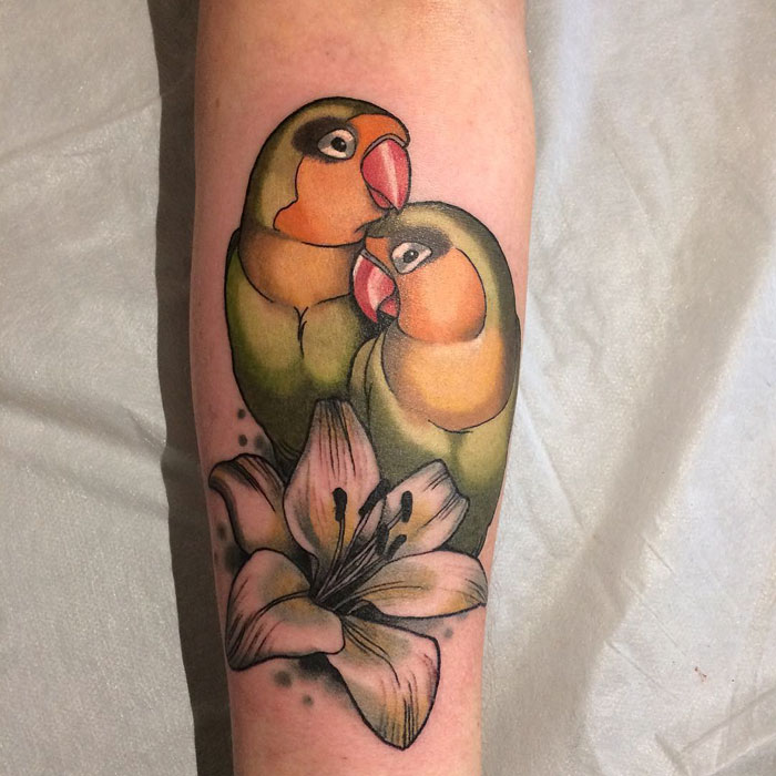 Colorful small bird tattoo featuring two vibrant parrots perched above a flower.