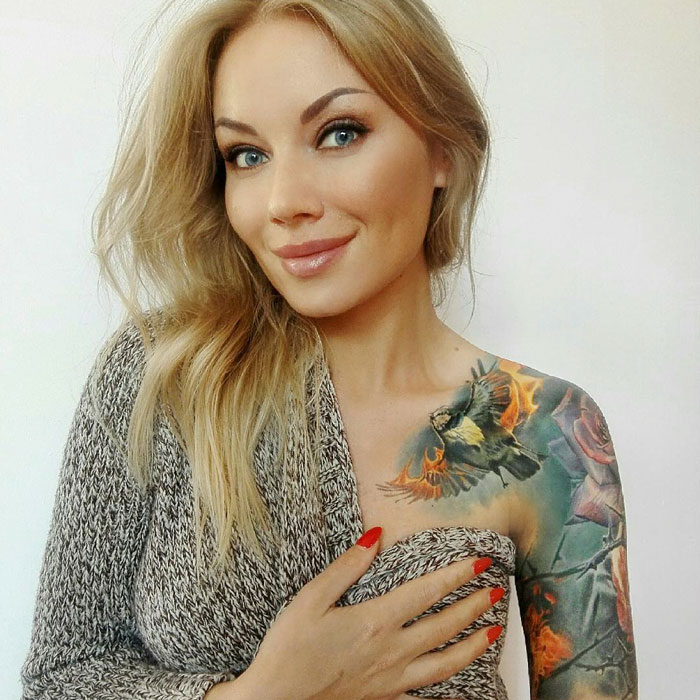 Woman showing colorful small bird tattoo on shoulder in a casual setting.