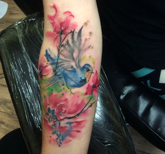 Colorful small bird tattoo with watercolor effect on arm.