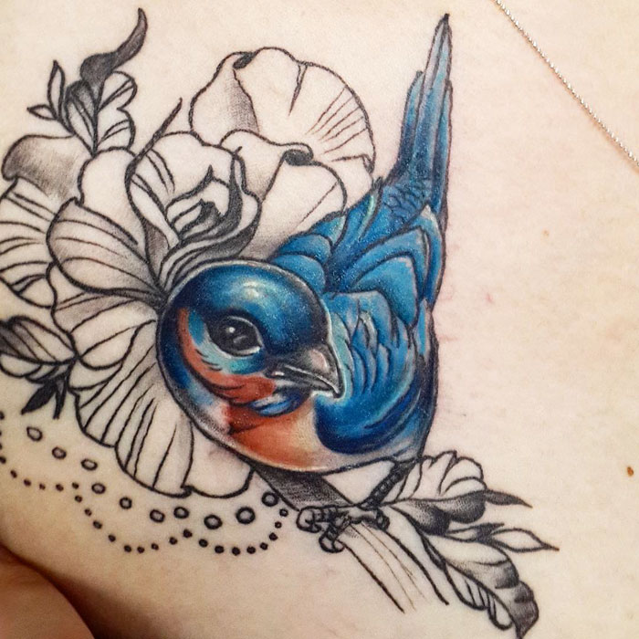 Colorful small bird tattoo with floral accents, showcasing unique tattoo art inspiration.