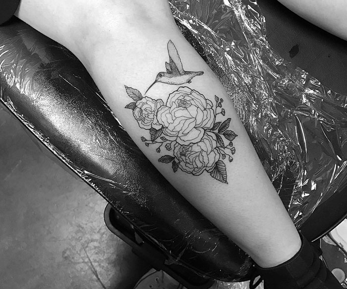 Small bird tattoo featuring a hummingbird with roses on a person's leg, showcasing unique ink design.