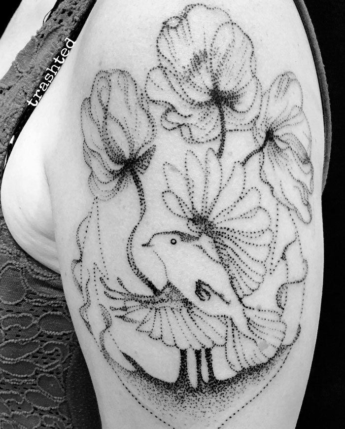 Unique small bird tattoo with floral design in detailed dot work on upper arm.