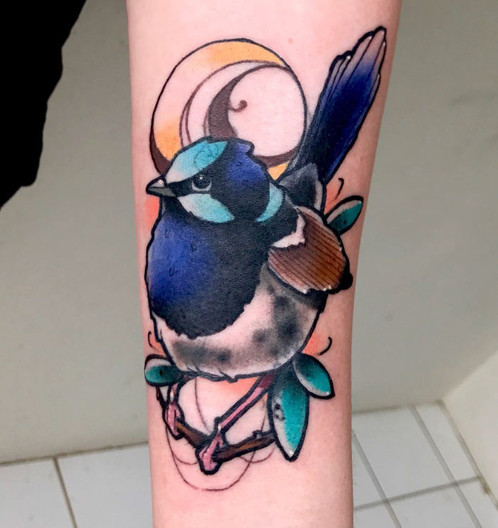 Colorful small bird tattoo with abstract elements on forearm.
