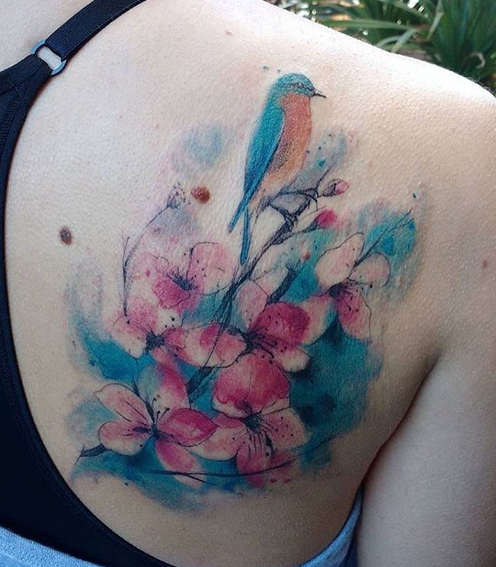 Colorful small bird tattoo with floral design on shoulder.