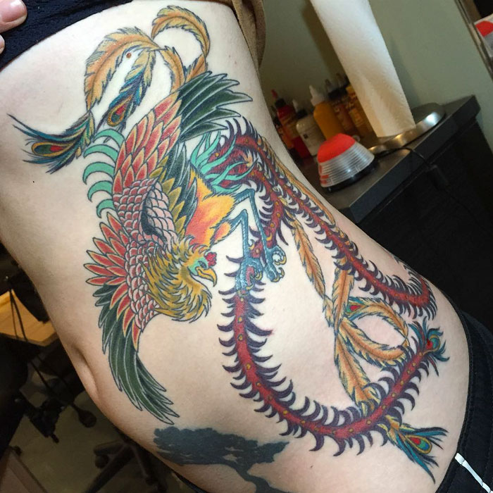 Colorful small bird tattoo featuring intricate designs on a person's side.