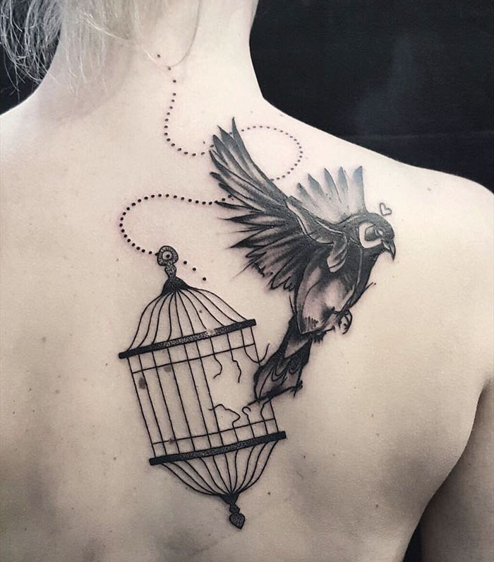 Unique small bird tattoo of a bird flying out of a cage on a person's back.