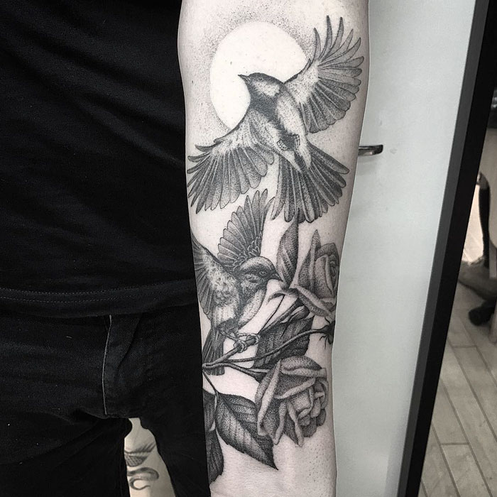 Detailed small bird tattoos with roses on forearm, showcasing artistic ink design.