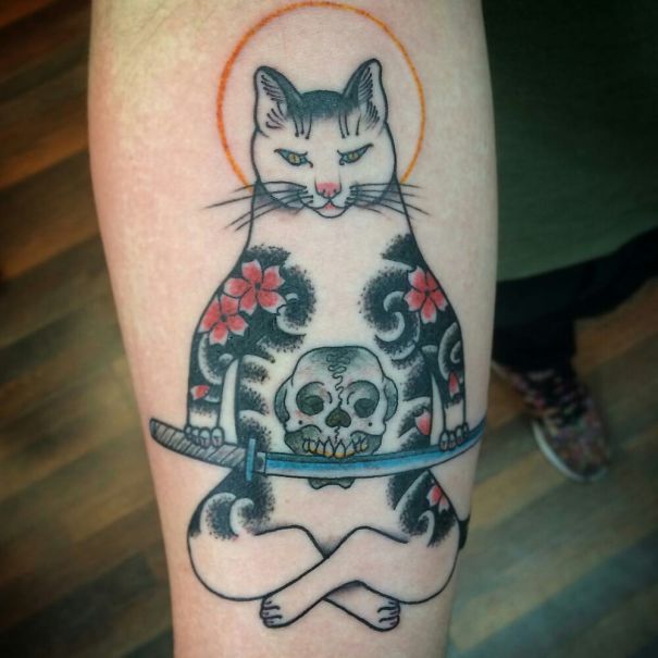 Cat tattoo design with floral patterns, a skull, and sword on a person's arm.