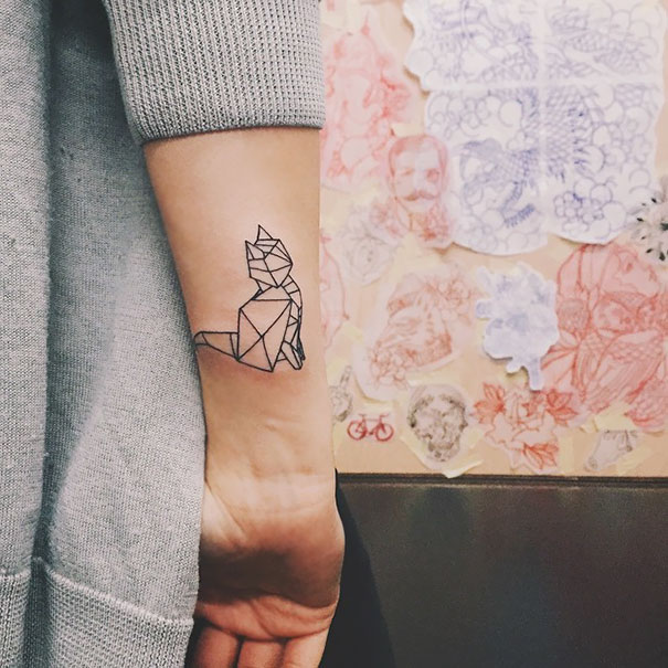 Geometric cat tattoo on the forearm of a person wearing a gray sweater, showcasing a unique cat person expression.