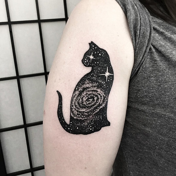 Galaxy-themed cat tattoo on arm, featuring a cosmic swirl and stars, perfect for cat lovers expressing themselves.