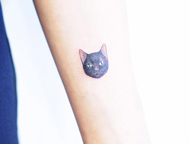Small black cat tattoo on a person's arm, representing cat lovers.