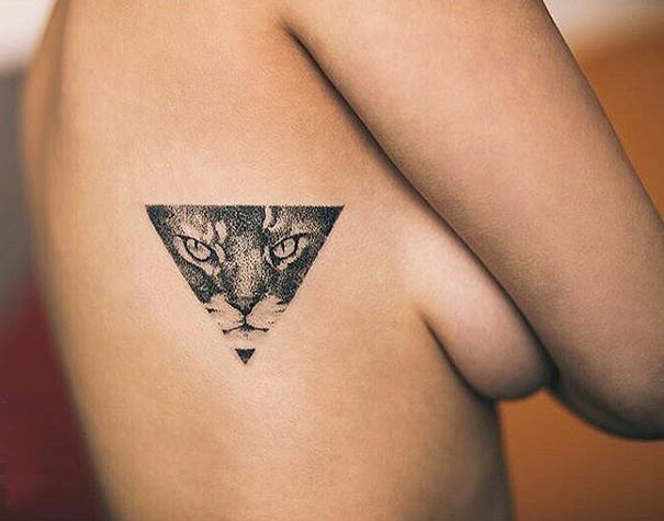 Cat tattoo design on a shoulder, featuring a triangular cat face illustration.