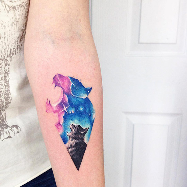 Colorful cat tattoo with galaxy design on forearm, featuring a howling wolf silhouette.