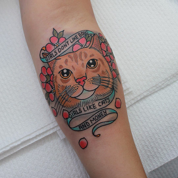 Cat tattoo with vibrant flowers and a playful phrase on a person's forearm, showcasing cat-themed body art.
