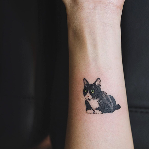 Cat tattoo on forearm featuring a black and white cat with green eyes, perfect for cat person self-expression.