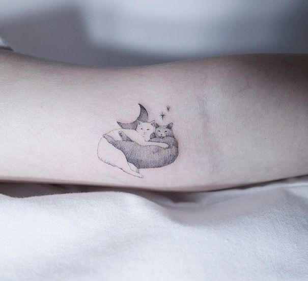 Minimalist cat tattoo featuring two cats cuddling under a crescent moon and stars.