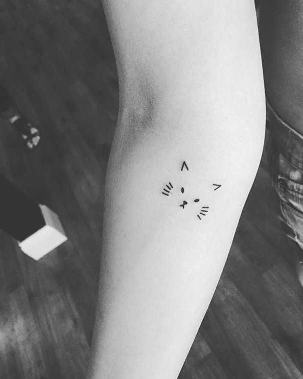 Minimalist cat tattoo on forearm, showcasing simple line art to express love for cats.