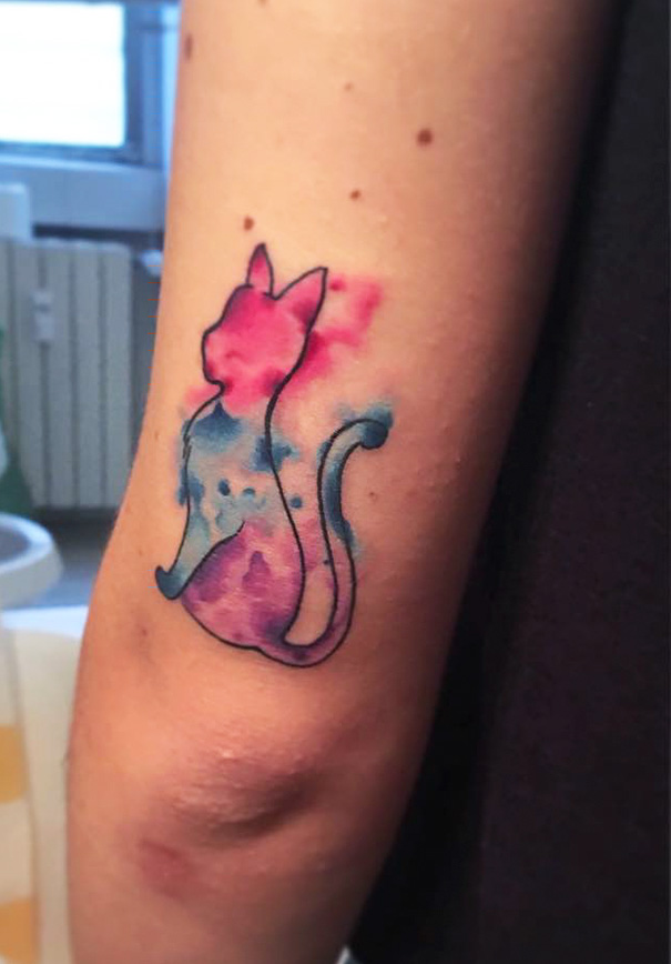 Watercolor cat tattoo on arm, showcasing vibrant pink and blue hues, perfect for cat lovers.