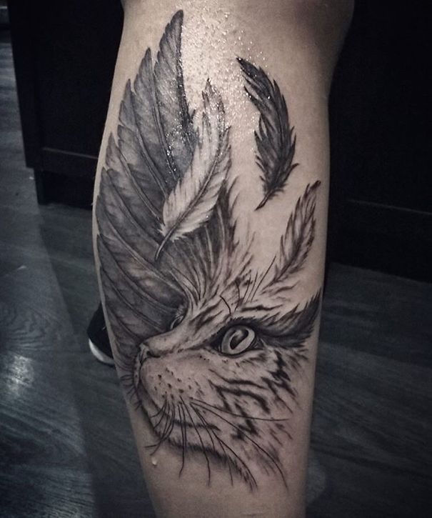 Artistic cat tattoo incorporating feathers on the thigh, showcasing creativity and passion for feline-inspired body art.