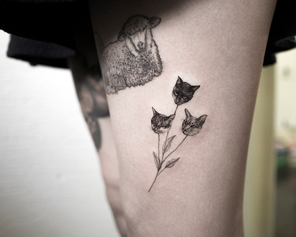 Cat tattoo on thigh featuring cat heads on a floral stem, showing unique cat person style.