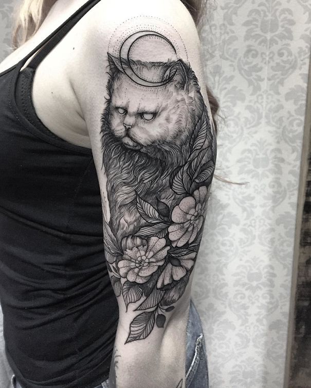 Cat tattoo on arm with floral elements and crescent moon design, showcasing intricate detail.