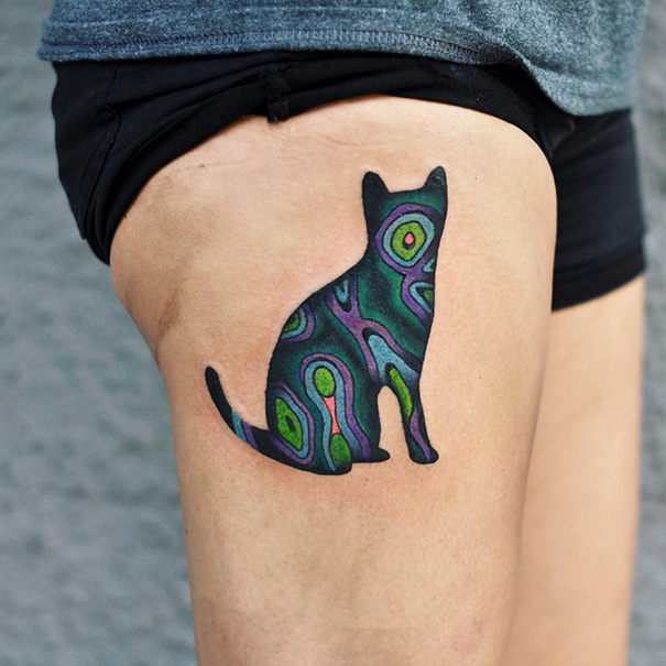 Colorful abstract cat tattoo on a person's thigh, showcasing a unique design for cat tattoo enthusiasts.