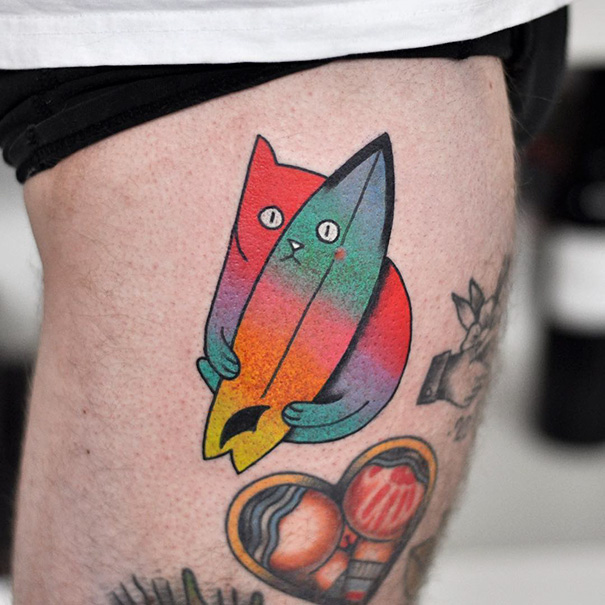 Colorful cat tattoo with a surfboard design on leg.