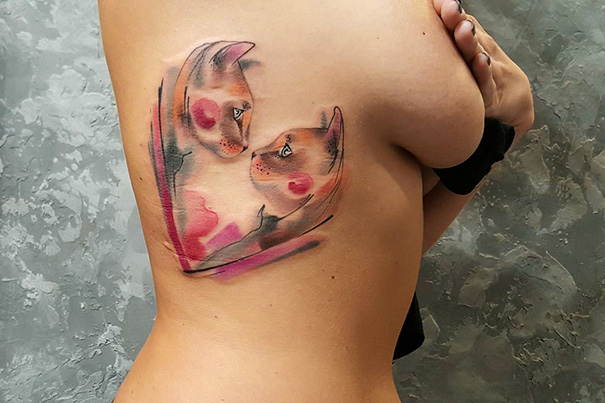 Watercolor cat tattoo on person's back, featuring two cats forming a heart shape.