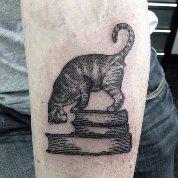 Cat tattoo of a feline balancing on stacked books, perfect for expressing yourself as a cat person.