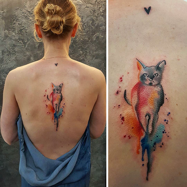 Watercolor cat tattoo on woman's back showcasing vibrant colors and feline design.